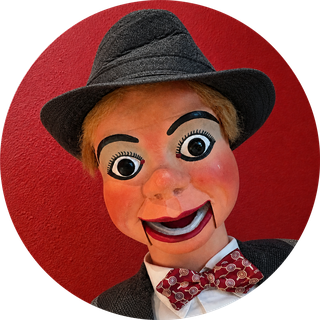 Dusty, a ventriloquial figure in a grey fedora and red bow tie