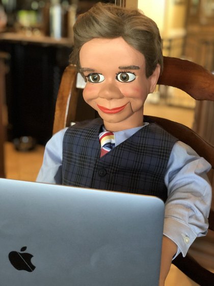 Freddy, a ventriloquial figure in a waistcoat and tie, seated at a laptop